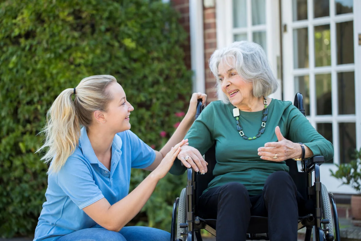 Cuidadora conversando con una residente en silla de ruedas, en el jardín de una residencia