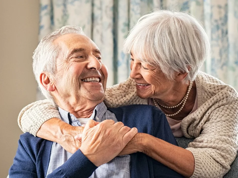 Pareja de adultos mayores sonriendo y abrazados en su hogar